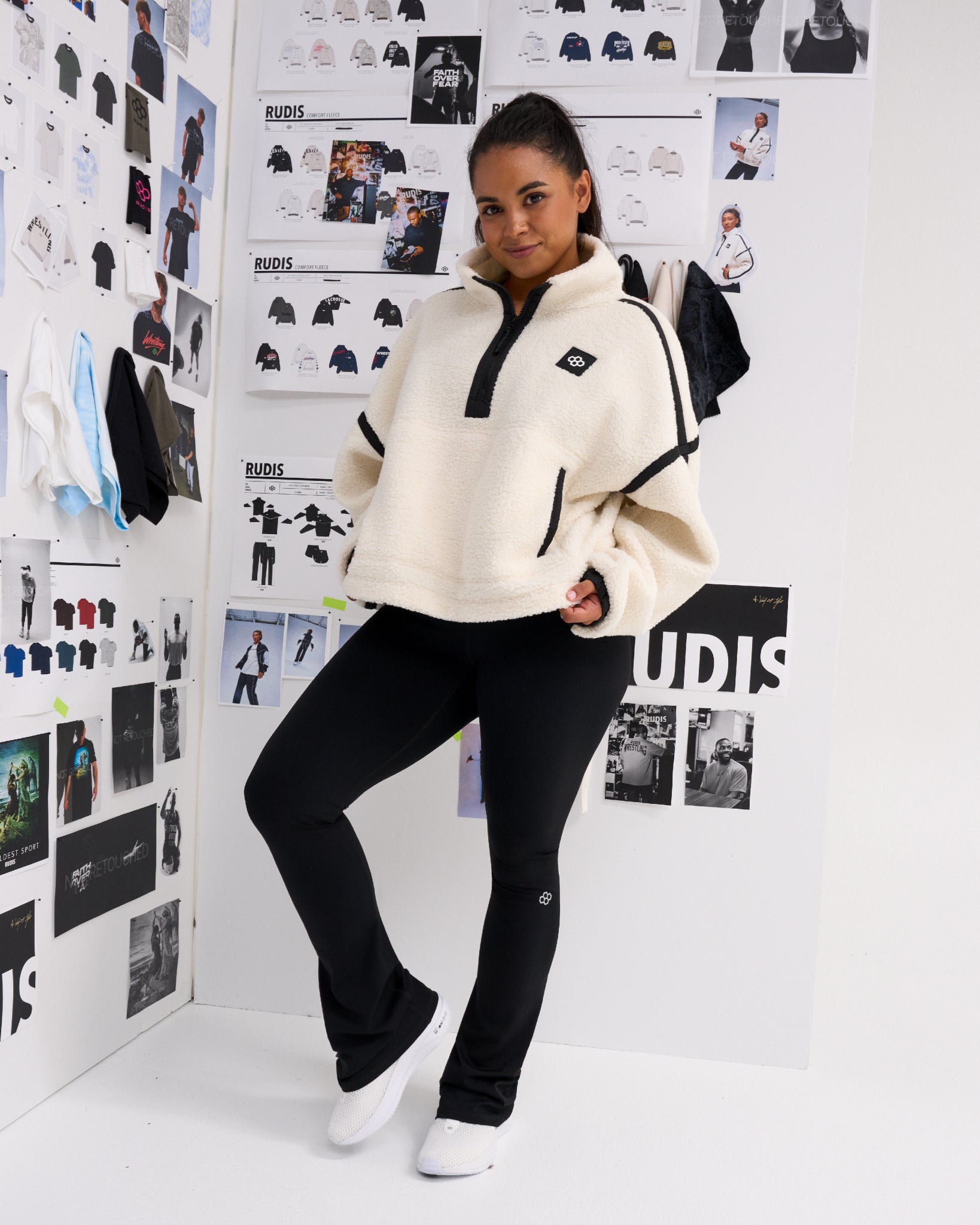 Model wearing the RUDIS Women's Sherpa Half Zip in White/Black with black leggings, showcasing the relaxed fit, half-zip collar, contrast piping and front pockets.