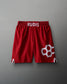 Red athletic shorts with a white 'RUDIS' logo on the waistband and interlocking hexagonal design on the side, set against a muted gray background.