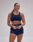 A woman modeling a matching navy blue activewear set consisting of a sports bra and athletic shorts, photographed against a neutral gray studio background.