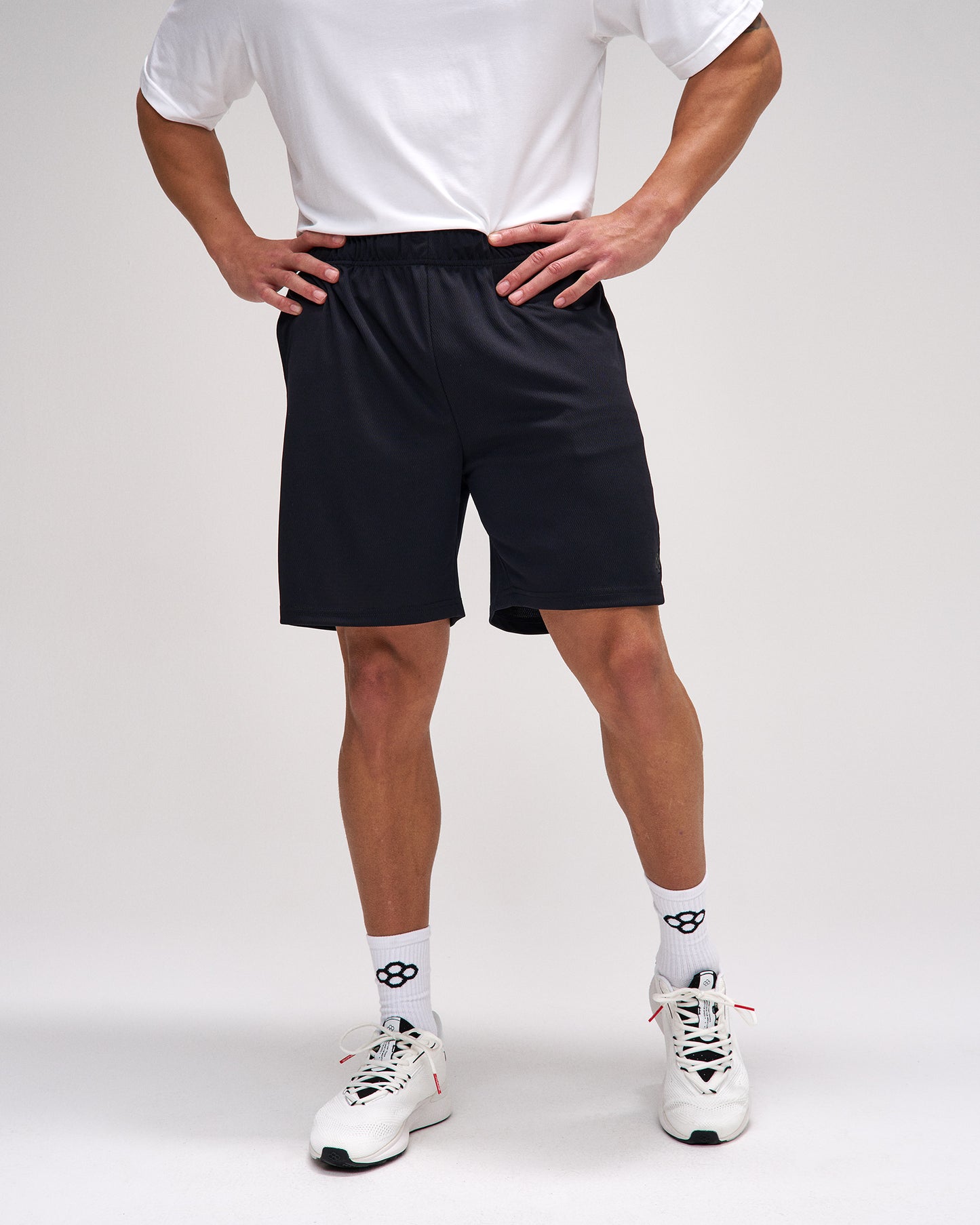Person wearing black shorts, white socks, and white sneakers on a plain background