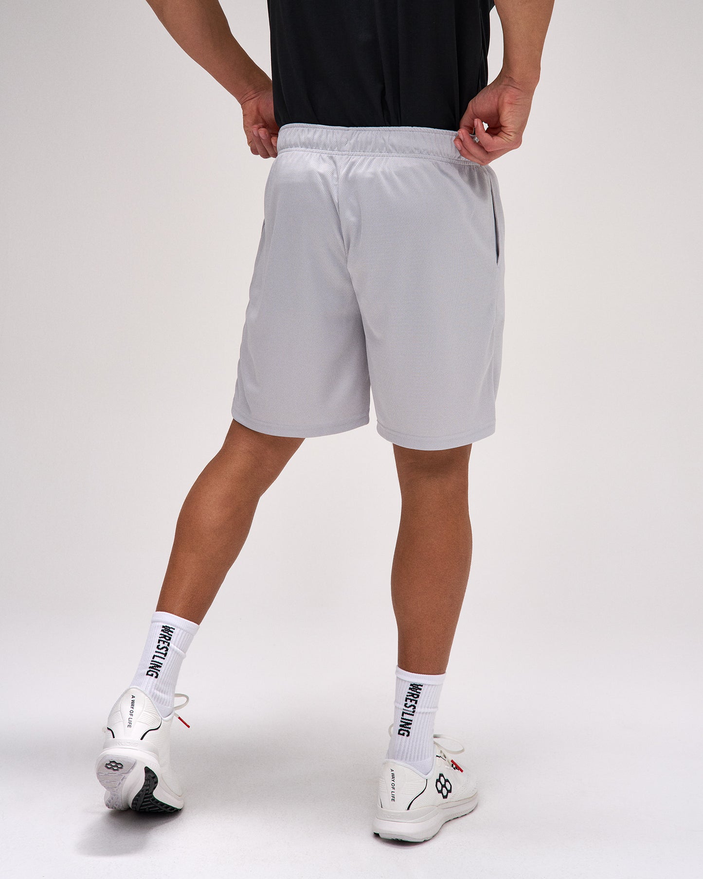 Person wearing gray shorts and white sneakers on a plain background