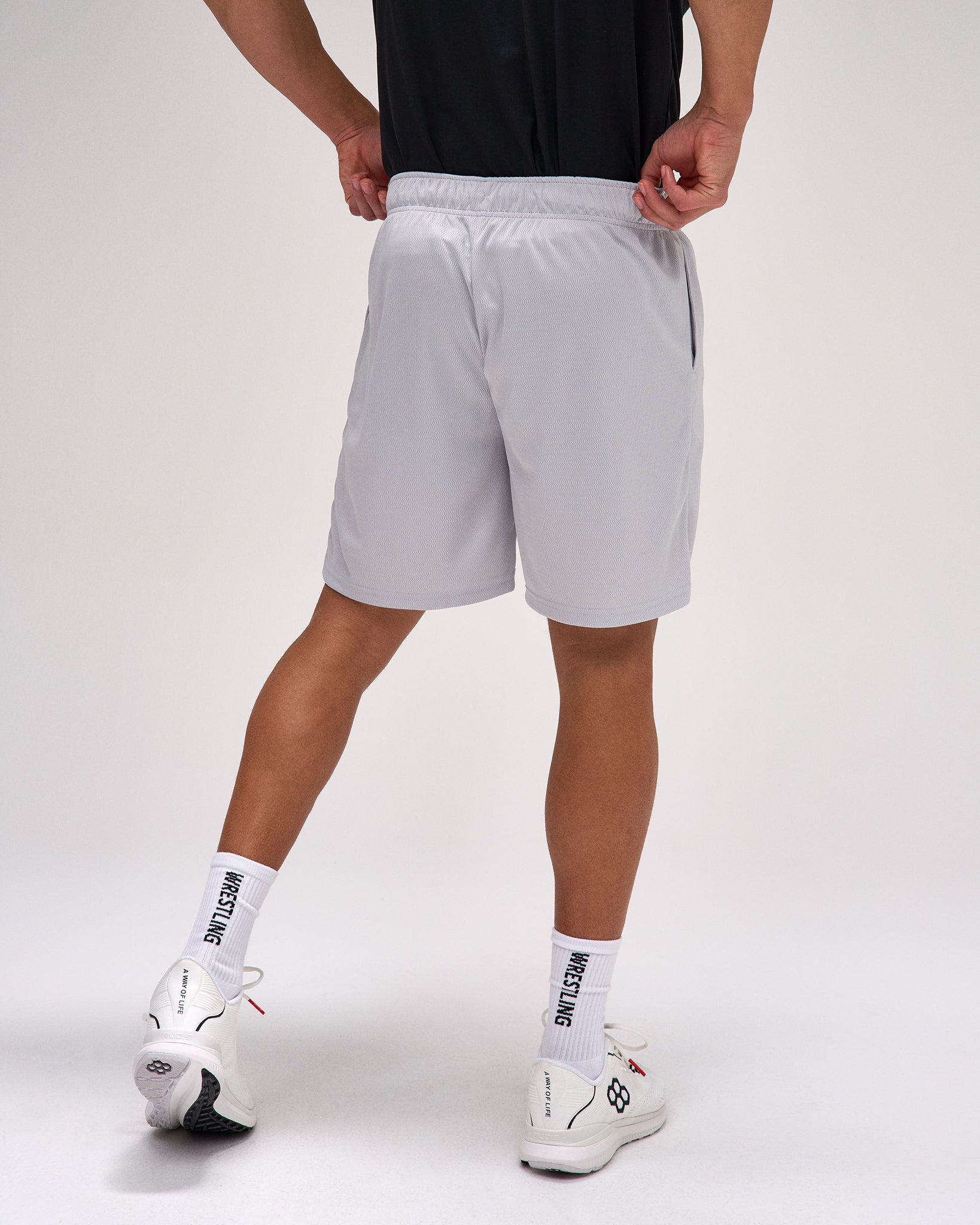 Person wearing gray shorts and white sneakers on a plain background
