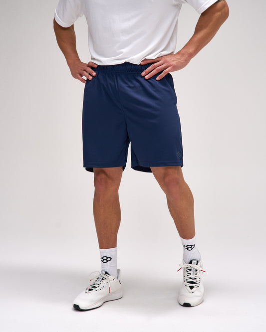 Person wearing navy shorts, white shirt, and white sneakers on a plain background