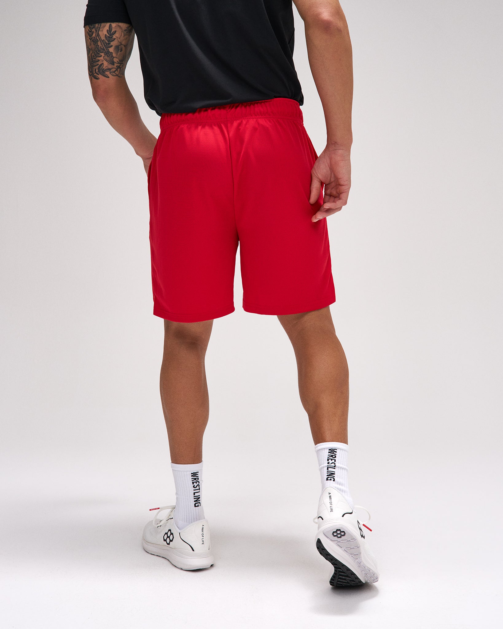 Person wearing red shorts, black shirt, white socks, and white sneakers on a light gray background