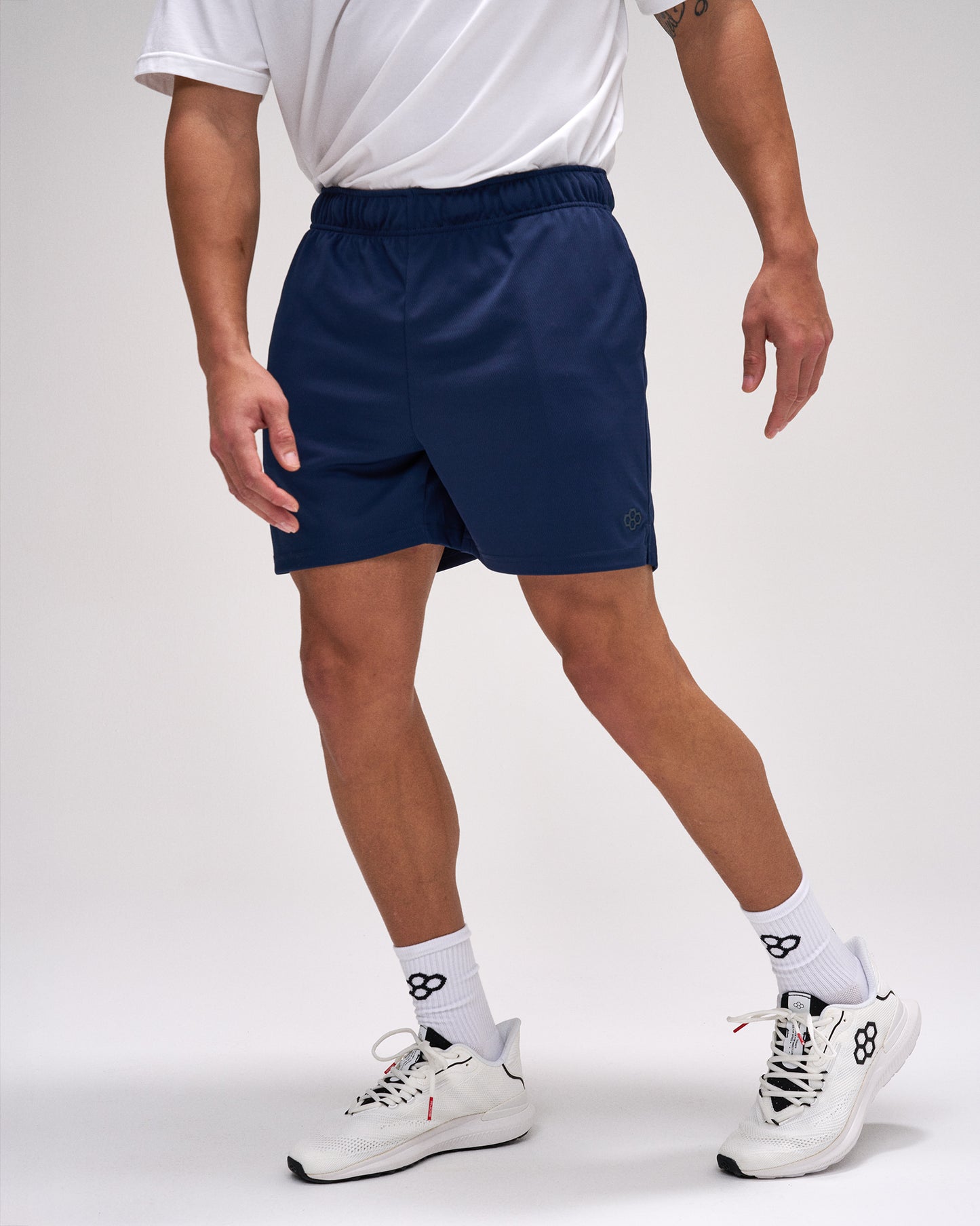 Person wearing navy shorts and white sneakers on a plain background