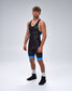 A male model wearing a black wrestling singlet with a subtle tonal pattern and bright blue accents on the sides and upper thighs, paired with white socks and black running shoes, against a light gray studio background.