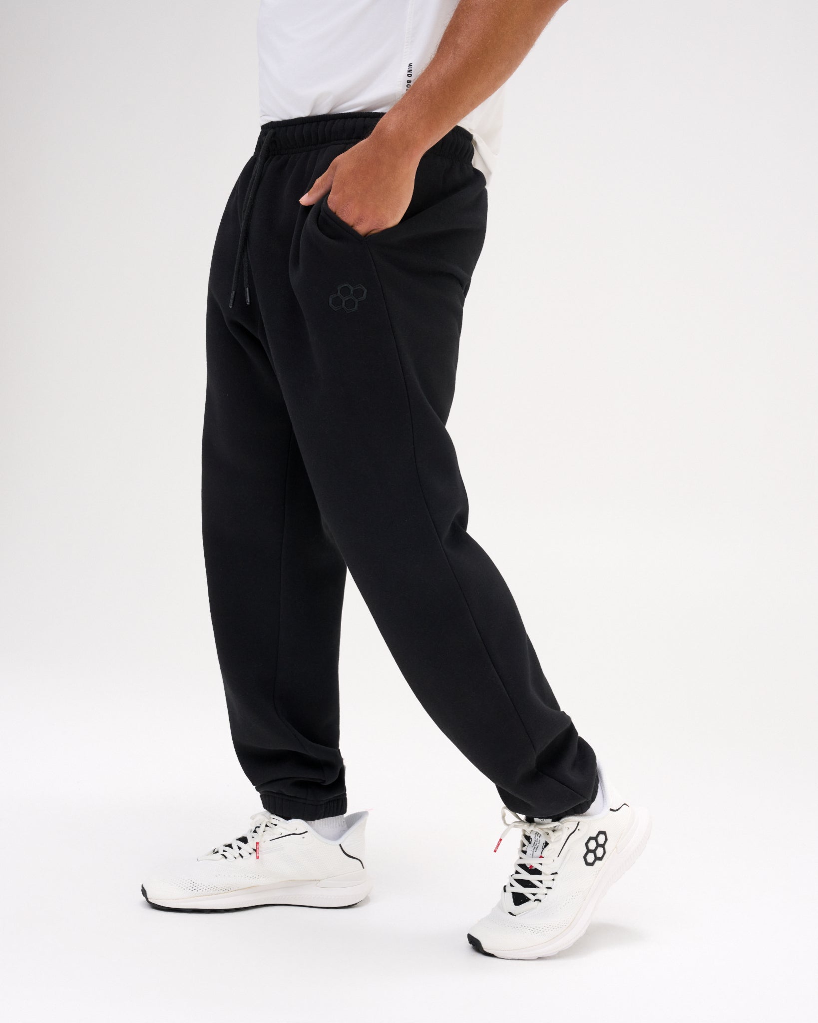 Side view of a model wearing RUDIS Comfort Fleece Baggy Sweatpants in Black, featuring a relaxed fit, adjustable drawstring waistband, side pockets, subtle RUDIS logo and elastic ankle cuffs.