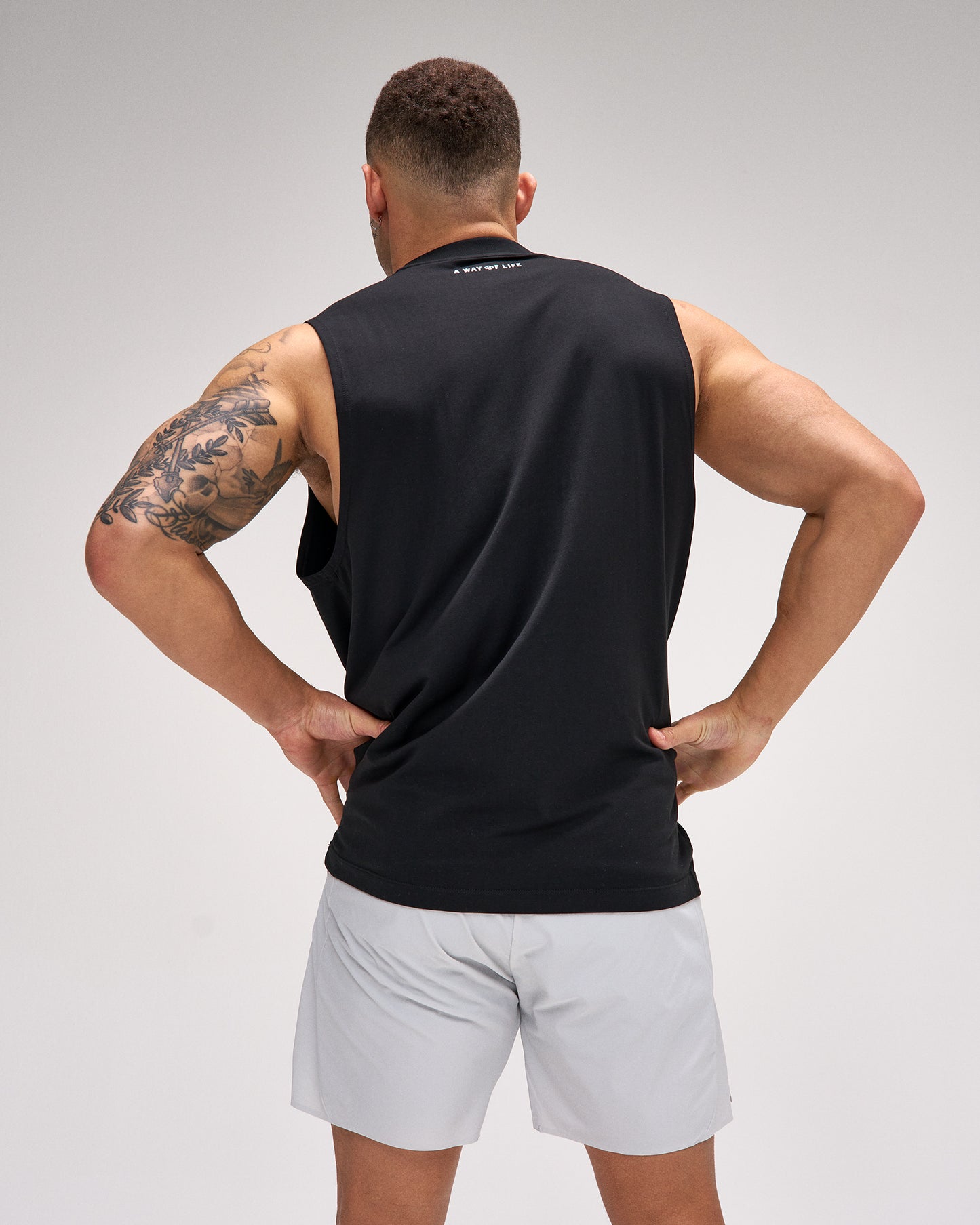 Man wearing a black sleeveless shirt and light gray shorts on a plain background