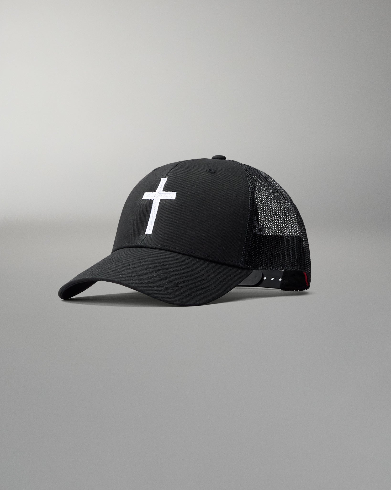 Front angled view of the RUDIS Fearless Faith Bridge Trucker Hat in Black, featuring an embroidered white cross, curved brim and breathable black mesh panels.