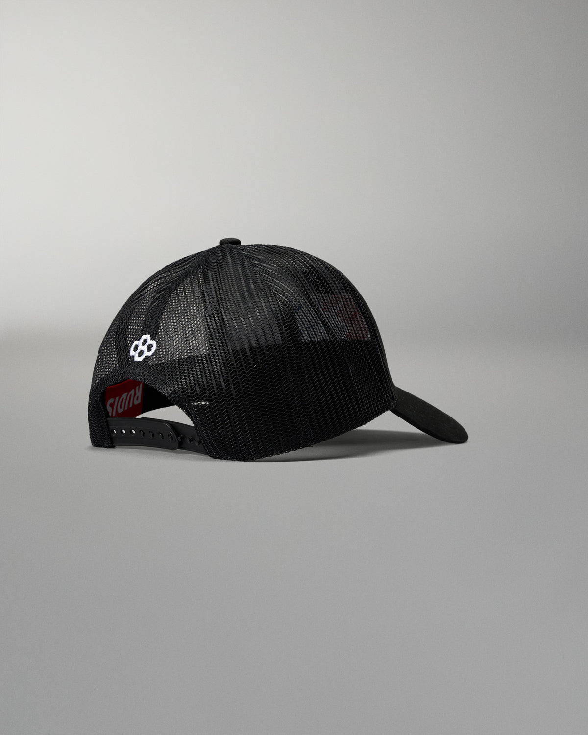 Rear angled view of the RUDIS Fearless Faith Bridge Trucker Hat in Black, showcasing breathable mesh panels, adjustable snapback closure and white embroidered RUDIS emblem.