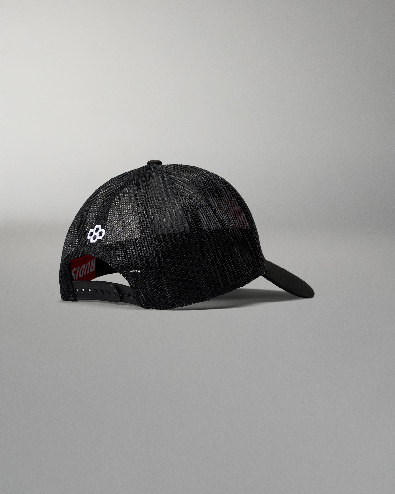 Rear angled view of the RUDIS Fearless Faith Bridge Trucker Hat in Black, showcasing breathable mesh panels, adjustable snapback closure and white embroidered RUDIS emblem.