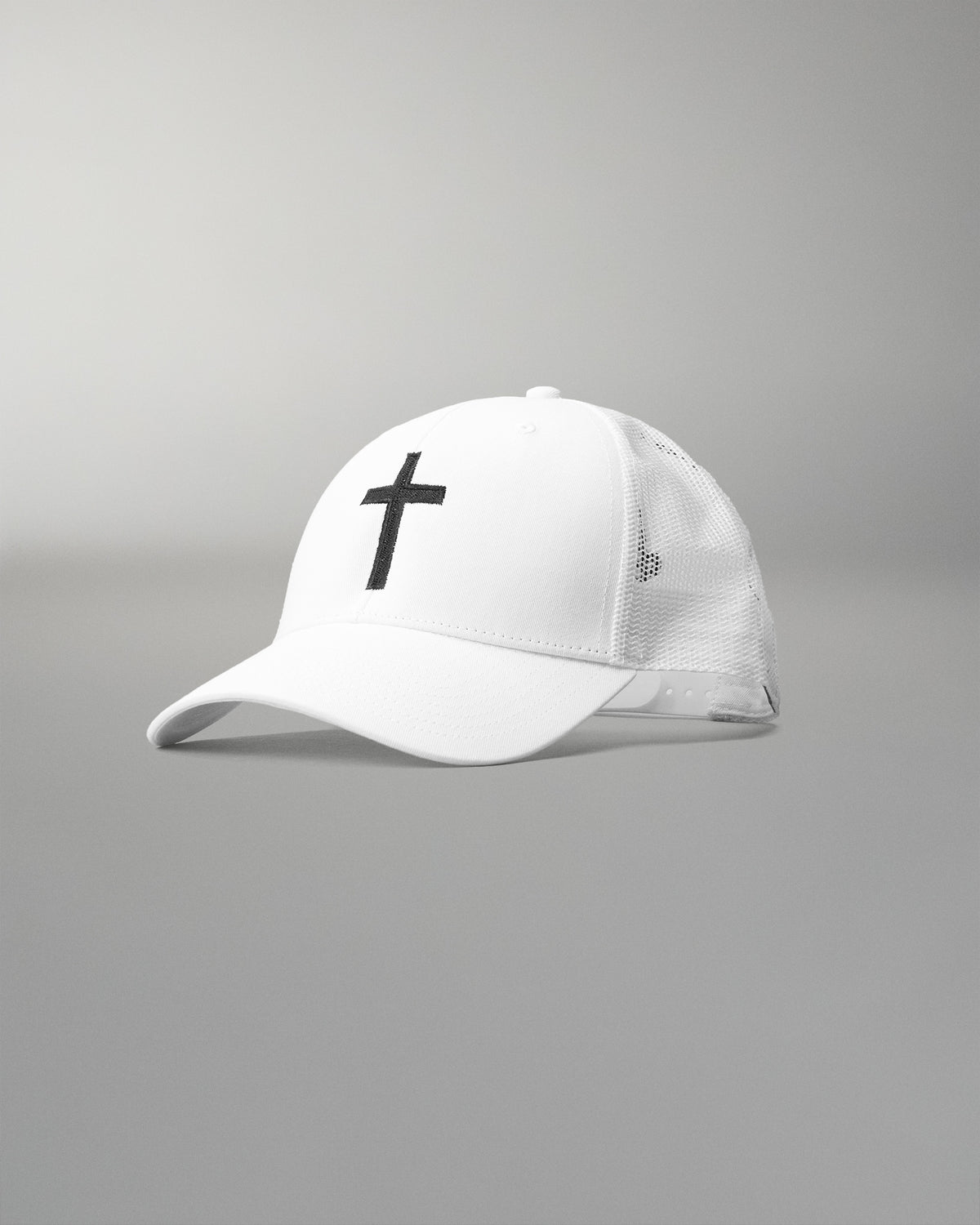 Front angled view of the RUDIS Fearless Faith Bridge Trucker Hat in White, featuring an embroidered black cross, curved brim and breathable white mesh panels.