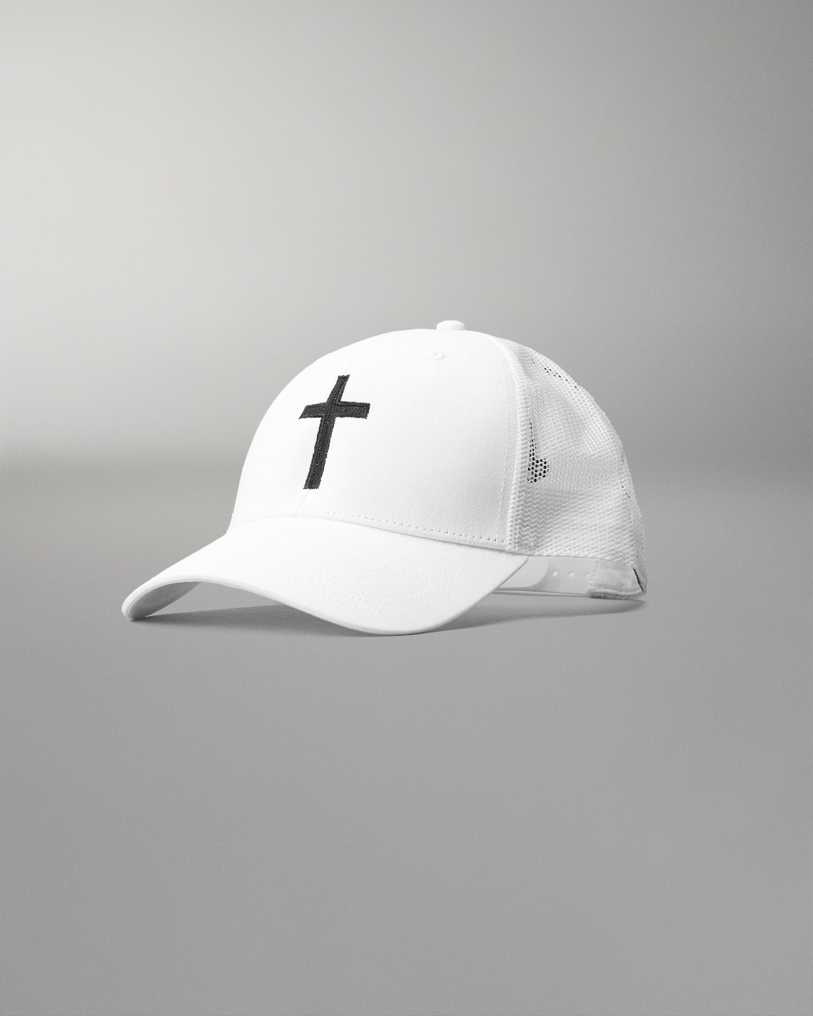 Front angled view of the RUDIS Fearless Faith Bridge Trucker Hat in White, featuring an embroidered black cross, curved brim and breathable white mesh panels.