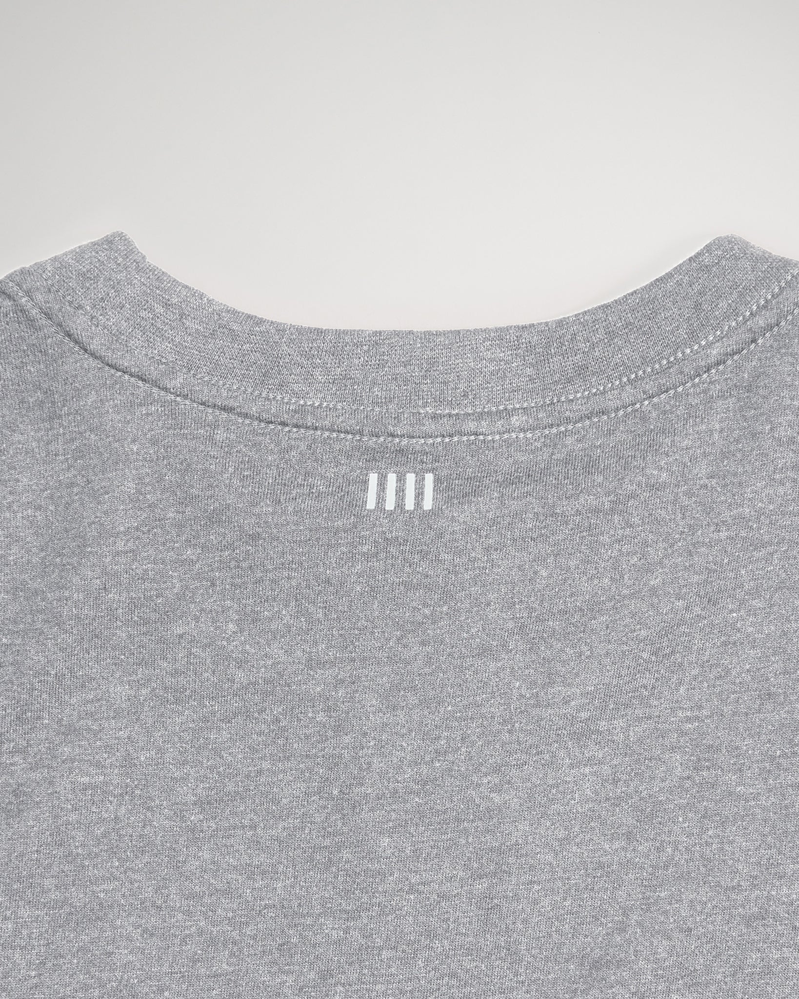 The back view of a gray T-shirt featuring a rounded neckline and three vertical white lines positioned near the collar indicating a simple yet modern design