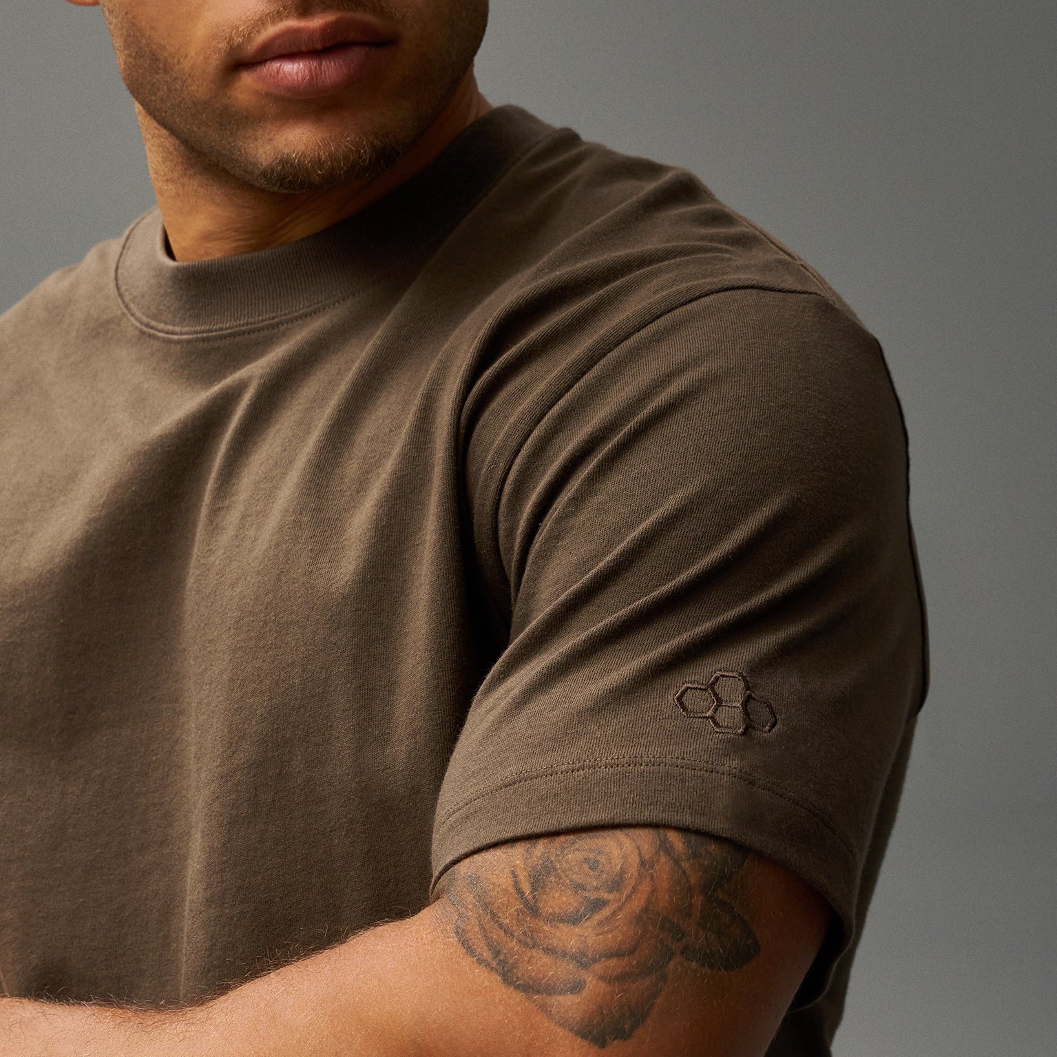Man wearing a brown RUDIS t-shirt with a logo on a gray background