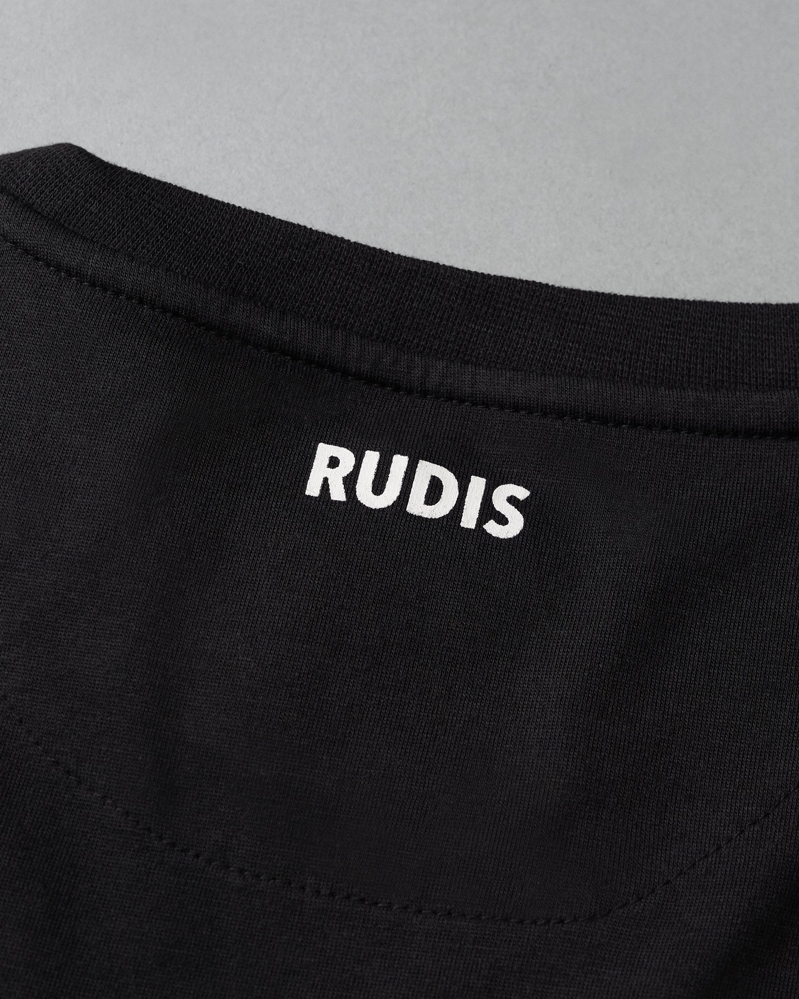 Close-up of a black garment with 'RUDIS' branding on a gray background