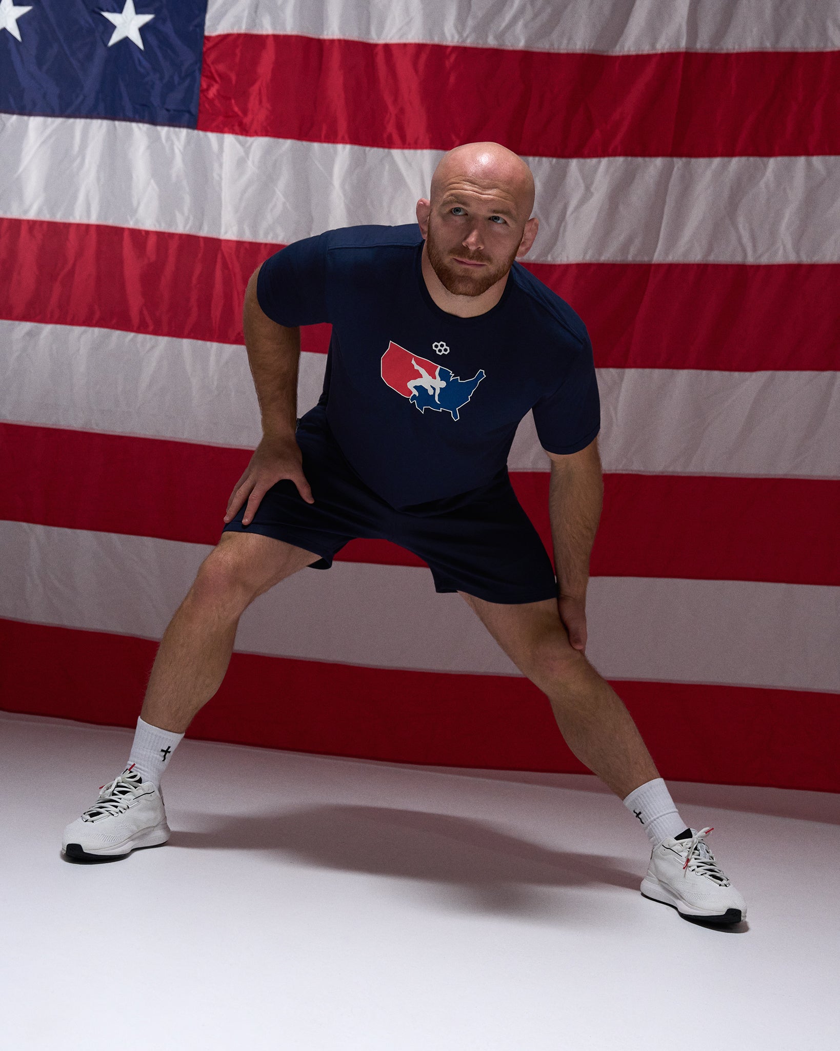 Athlete stretching in the RUDIS USA Wrestling T-Shirt in navy with matching athletic shorts, posed in front of an American flag.