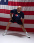 Athlete stretching in the RUDIS USA Wrestling T-Shirt in navy with matching athletic shorts, posed in front of an American flag.