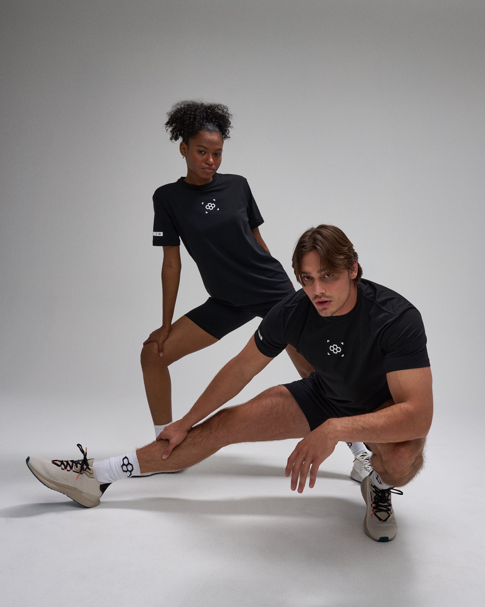 Two people wearing black athletic outfits with a logo on a white background