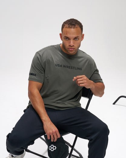 Man wearing a USA Wrestling t-shirt sitting on a chair against a white background