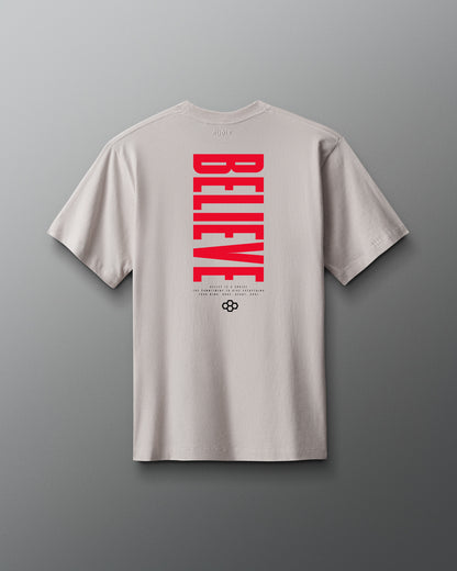 Beige t-shirt with red 'BELIEVE' text on the back against a gray background