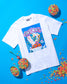 White t-shirt with a colorful graphic design on a blue background with cereal bowls.