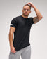 Man wearing a black t-shirt and gray pants against a plain background