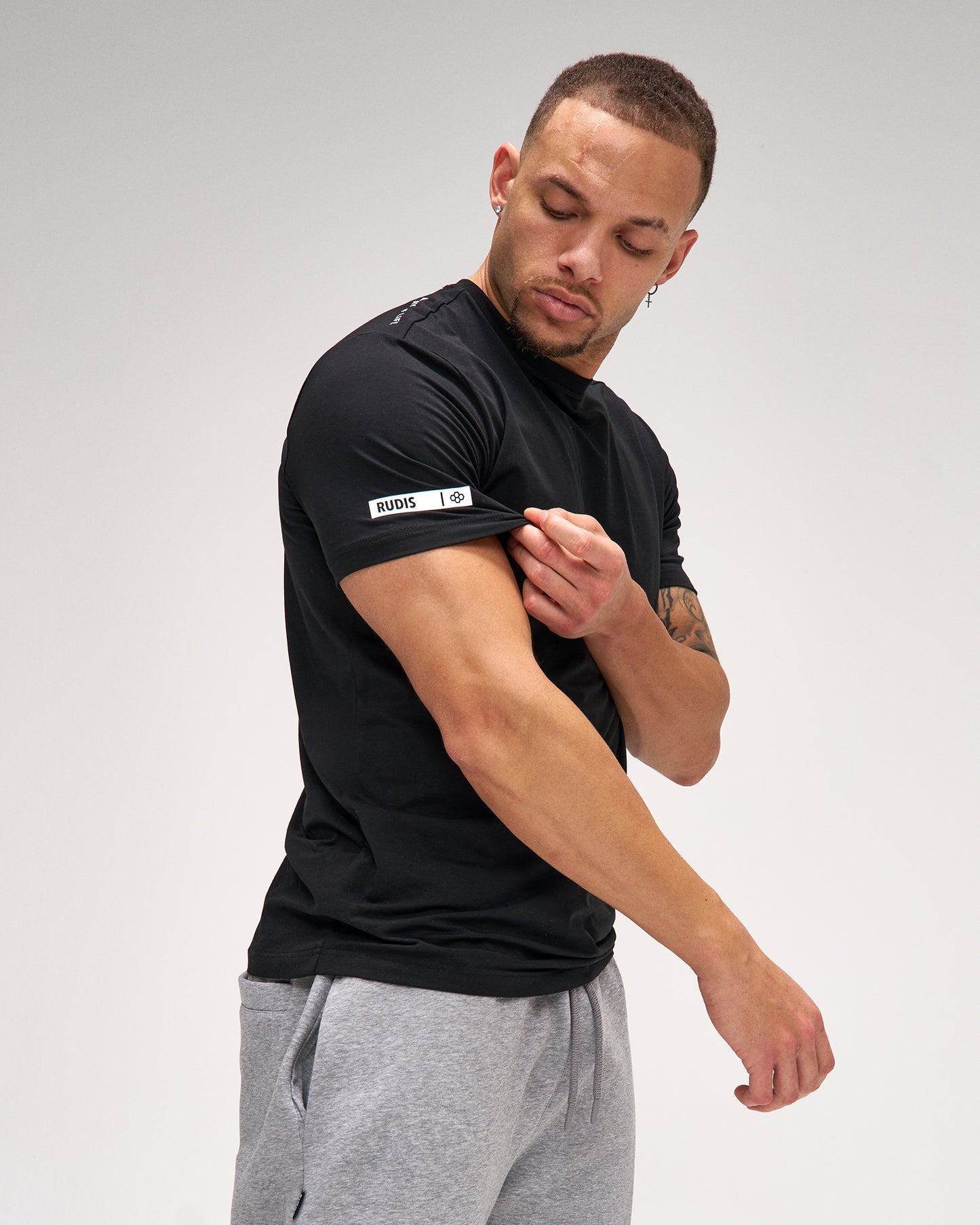 Man wearing a black t-shirt with a brand logo on a gray background