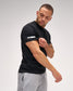 Man wearing a black t-shirt with a brand logo on a gray background