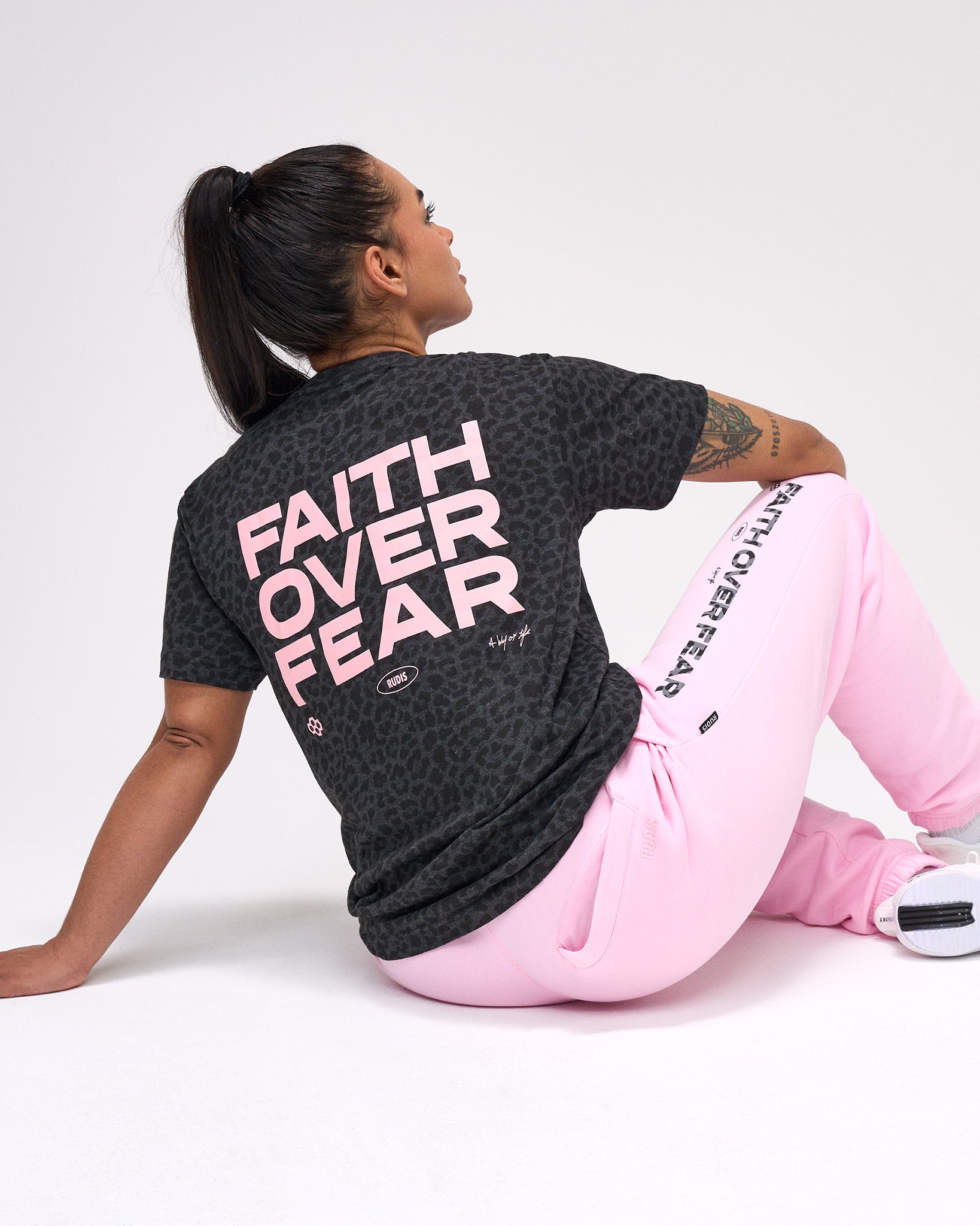 Person wearing a black animal printed t-shirt with 'Faith Over Fear' text, sitting on a white background