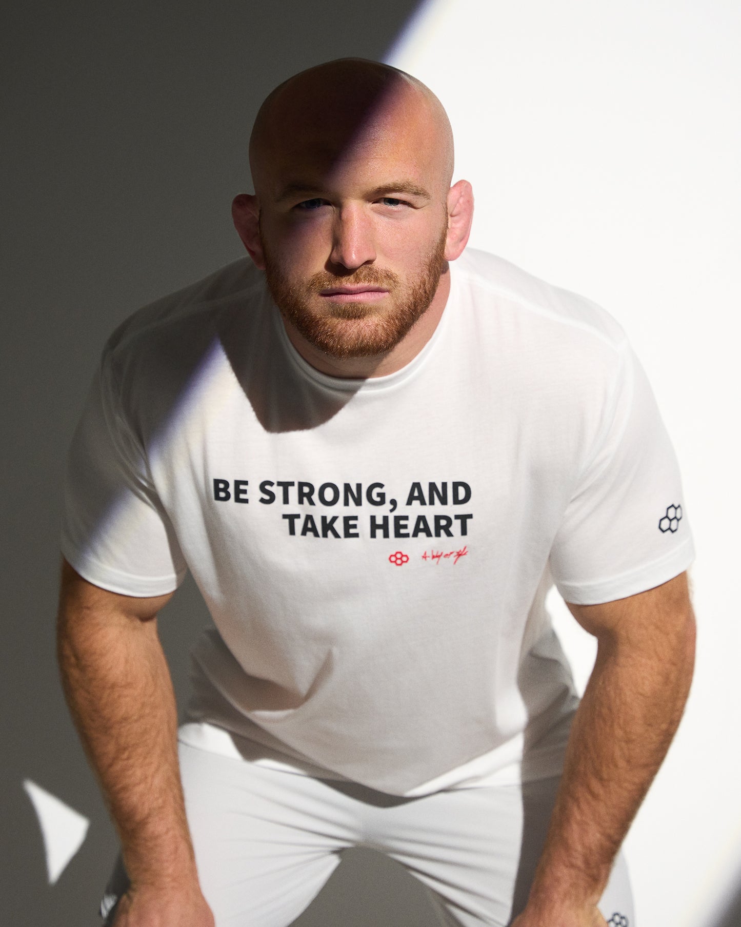 Athlete wearing the RUDIS Be Strong, Take Heart Elite Super Soft T-Shirt in white featuring bold motivational typography and premium everyday comfort.