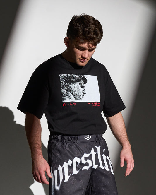 Person wearing a black t-shirt with graphic design and black pants with 'Wrestling' text.