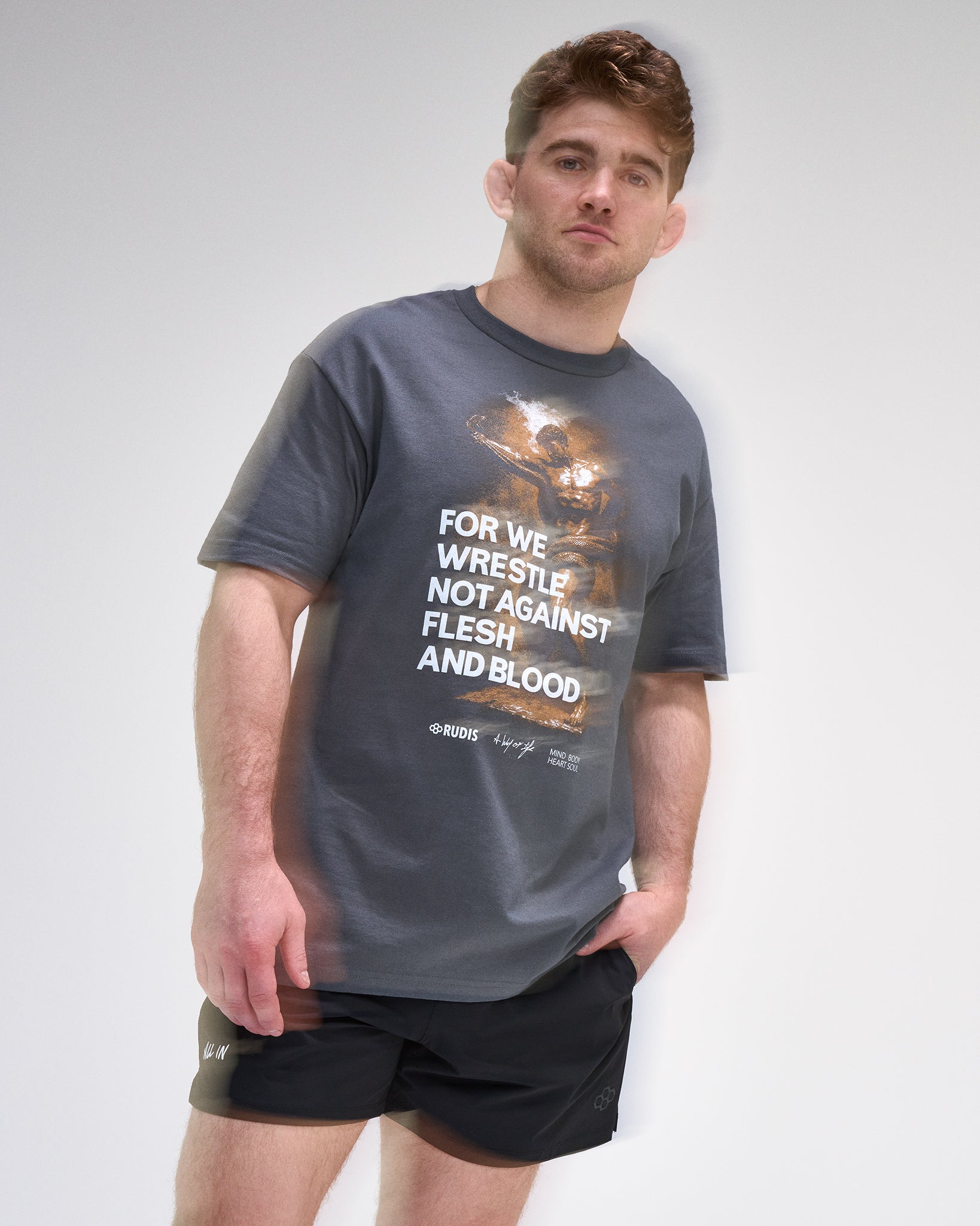 Man wearing a gray t-shirt with a graphic and 'For We Wrestle not against flesh and blood' text on a plain background