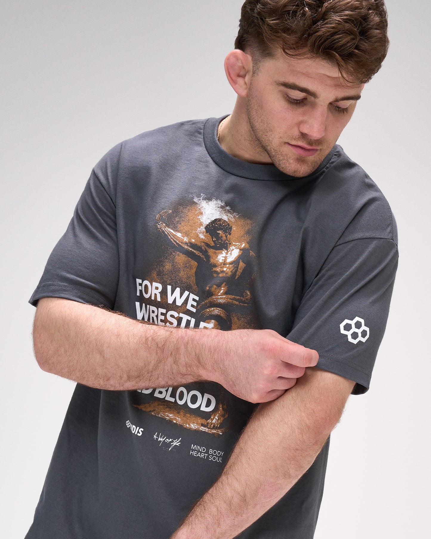 Man wearing a dark gray t-shirt with graphic design and "For we wrestle not against flesh and blood' text on a light gray background