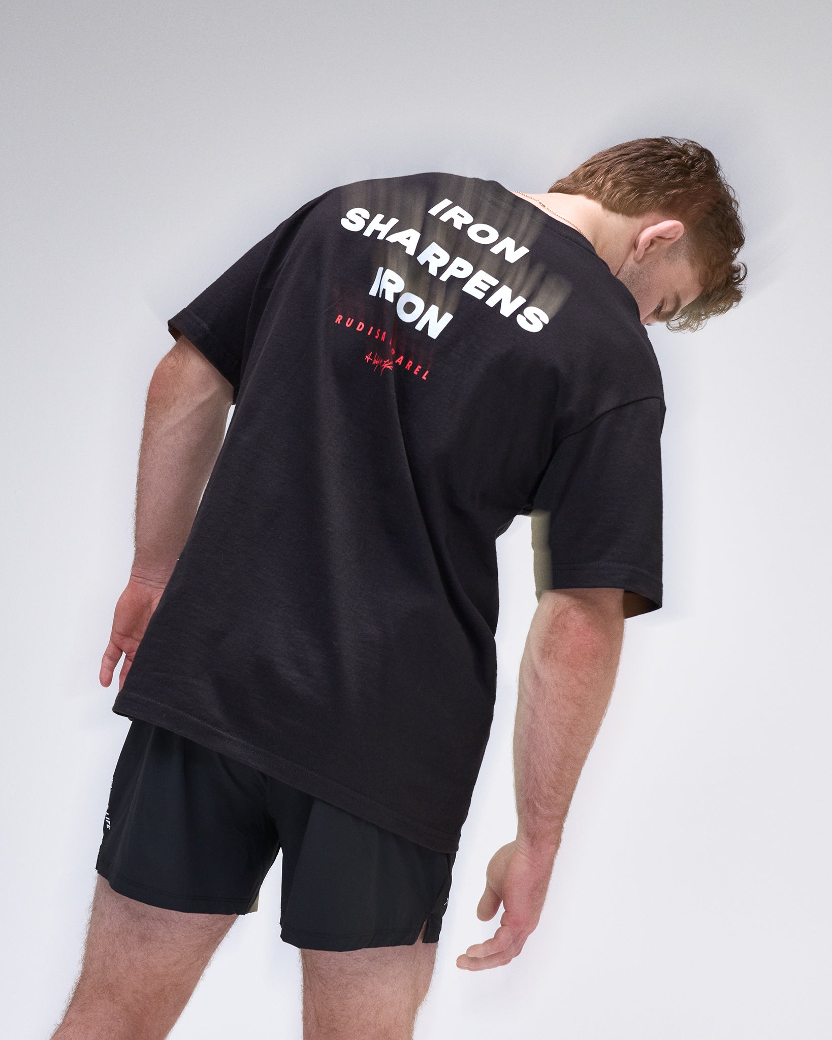 Person wearing a black t-shirt with 'Iron Sharpens Iron' text on the back against a white background