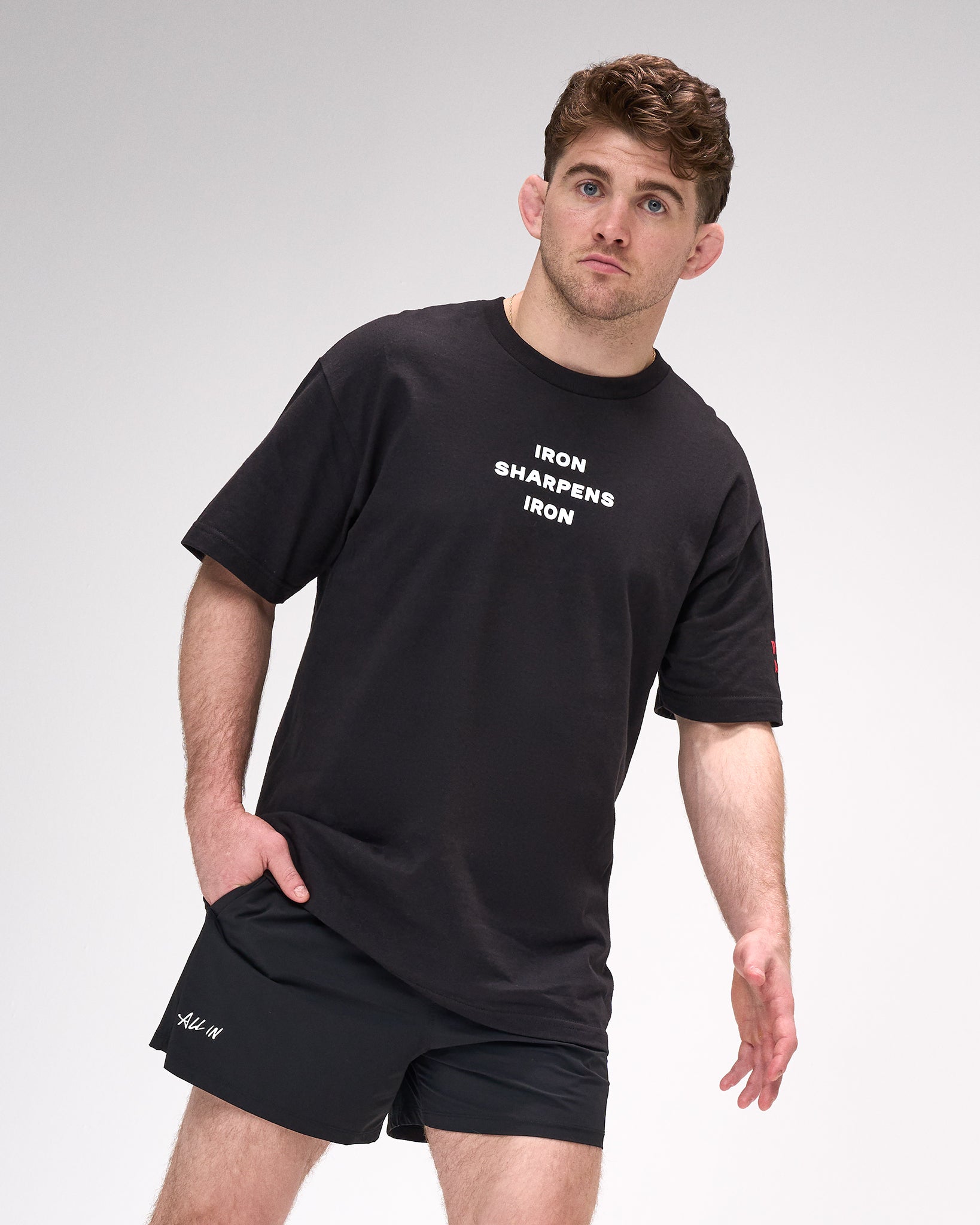 Man wearing a black t-shirt with 'IRON SHARPENS IRON' text and black shorts on a white background