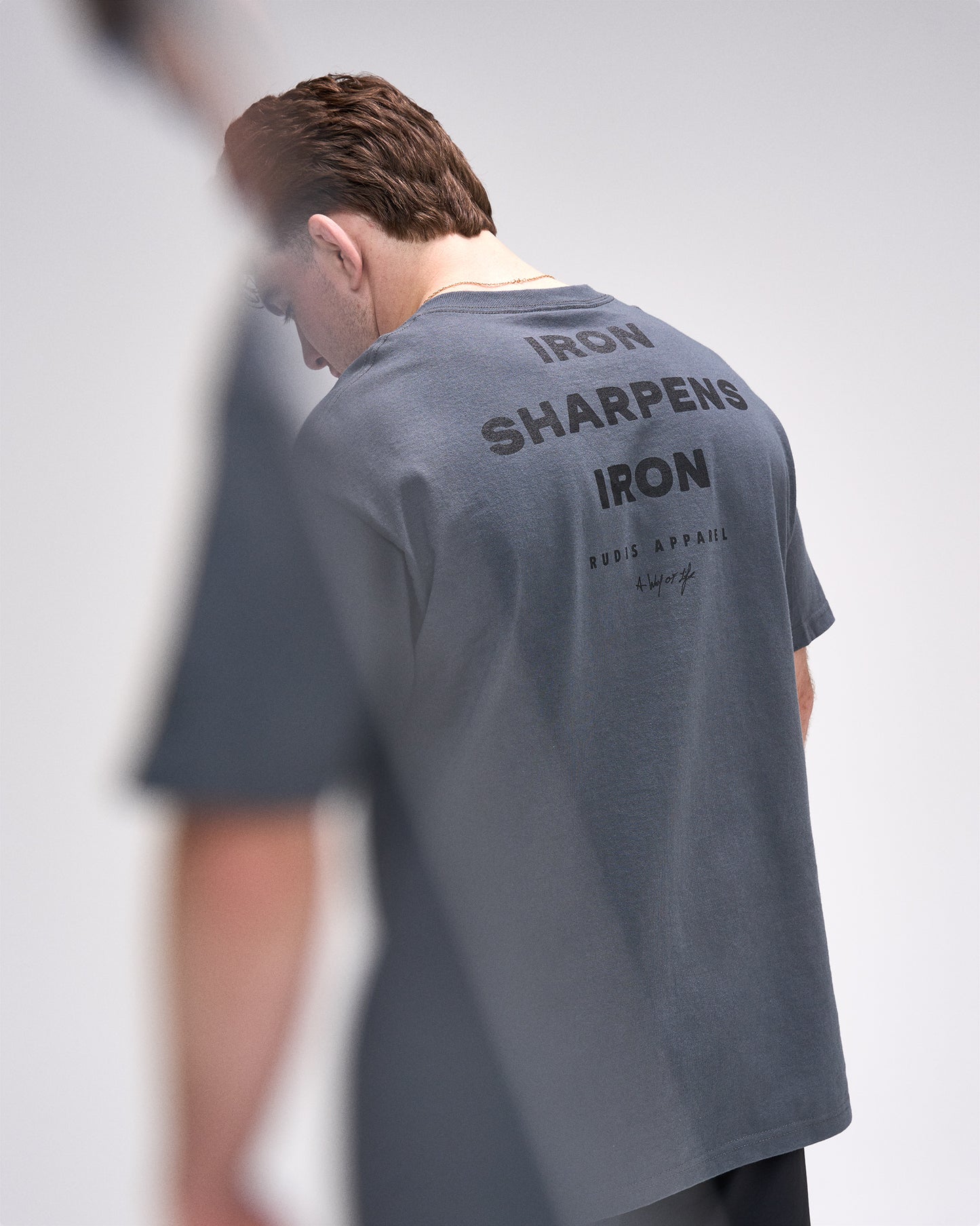 Person wearing a gray t-shirt with text on the back, standing against a plain background