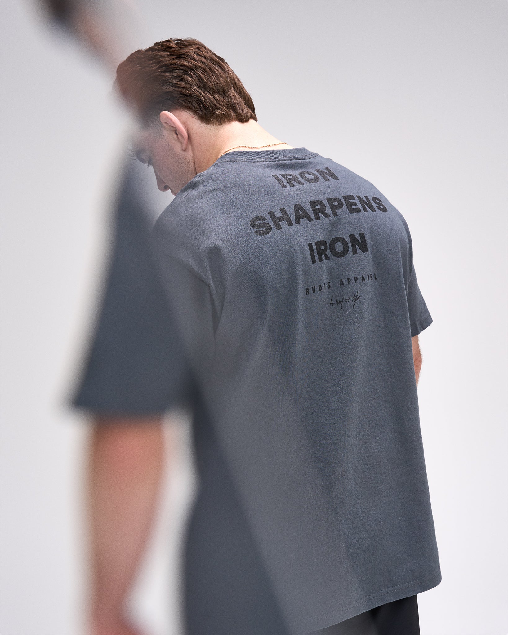Person wearing a gray t-shirt with text on the back, standing against a plain background