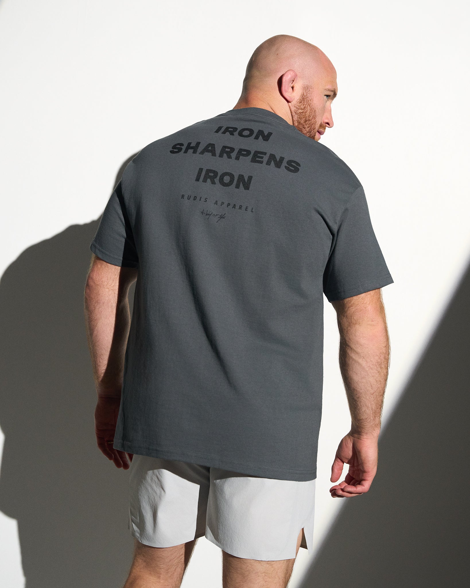Man wearing a gray t-shirt with 'IRON SHARPENS IRON' text on the back, standing against a white background.