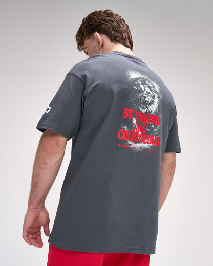 Man wearing a gray t-shirt with a lion graphic and 'Be strong and Courageous' text on the back, on a plain background