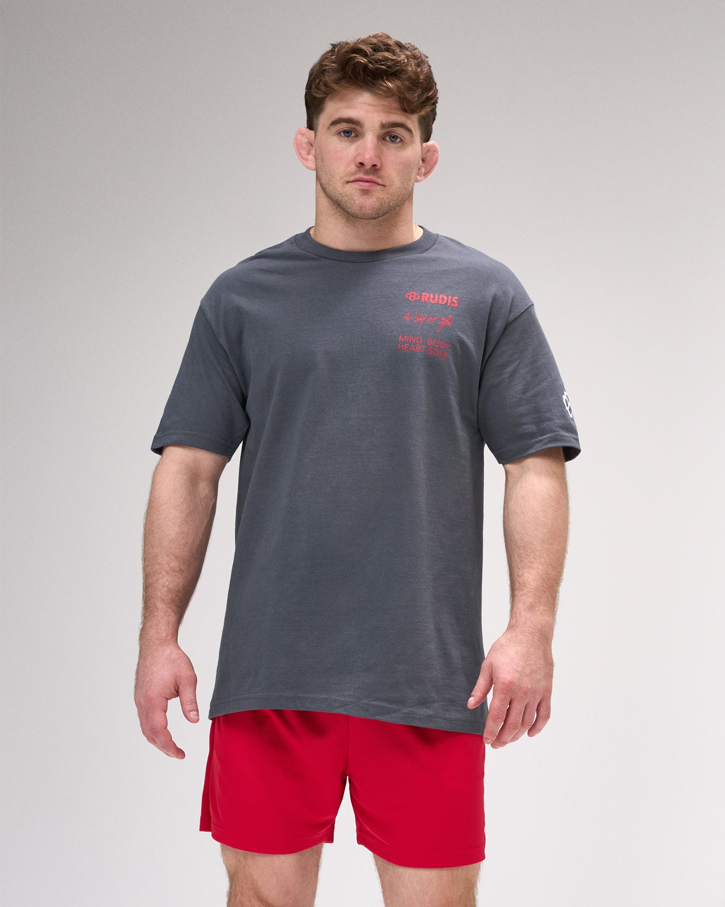 Man wearing a gray t-shirt with red text and red shorts on a gray background