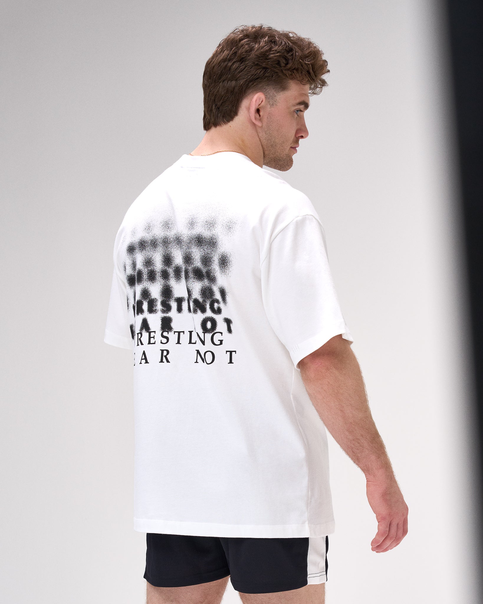 Man wearing a white t-shirt with 'Wrestling Fear not' text on the back, standing against a plain background