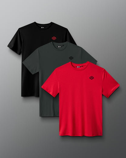 Three short-sleeve crew-neck T-shirts arranged in a fan layout on a gray gradient background: one black, one dark gray, and one bright red. Each shirt has a small geometric chest logo.