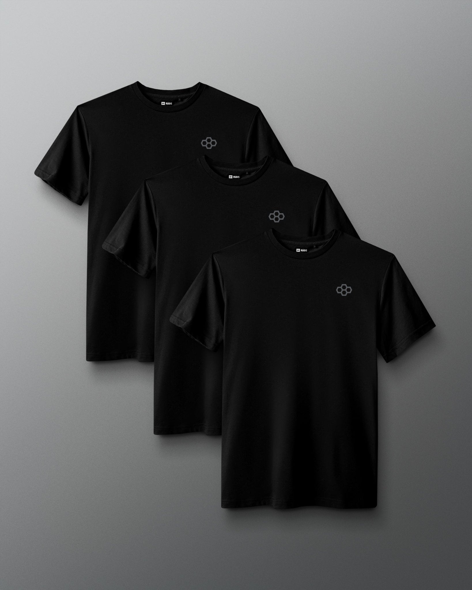 Three black short-sleeve crewneck t-shirts with a small white geometric logo on the left chest, arranged in a staggered overlapping layout on a dark gray gradient background.