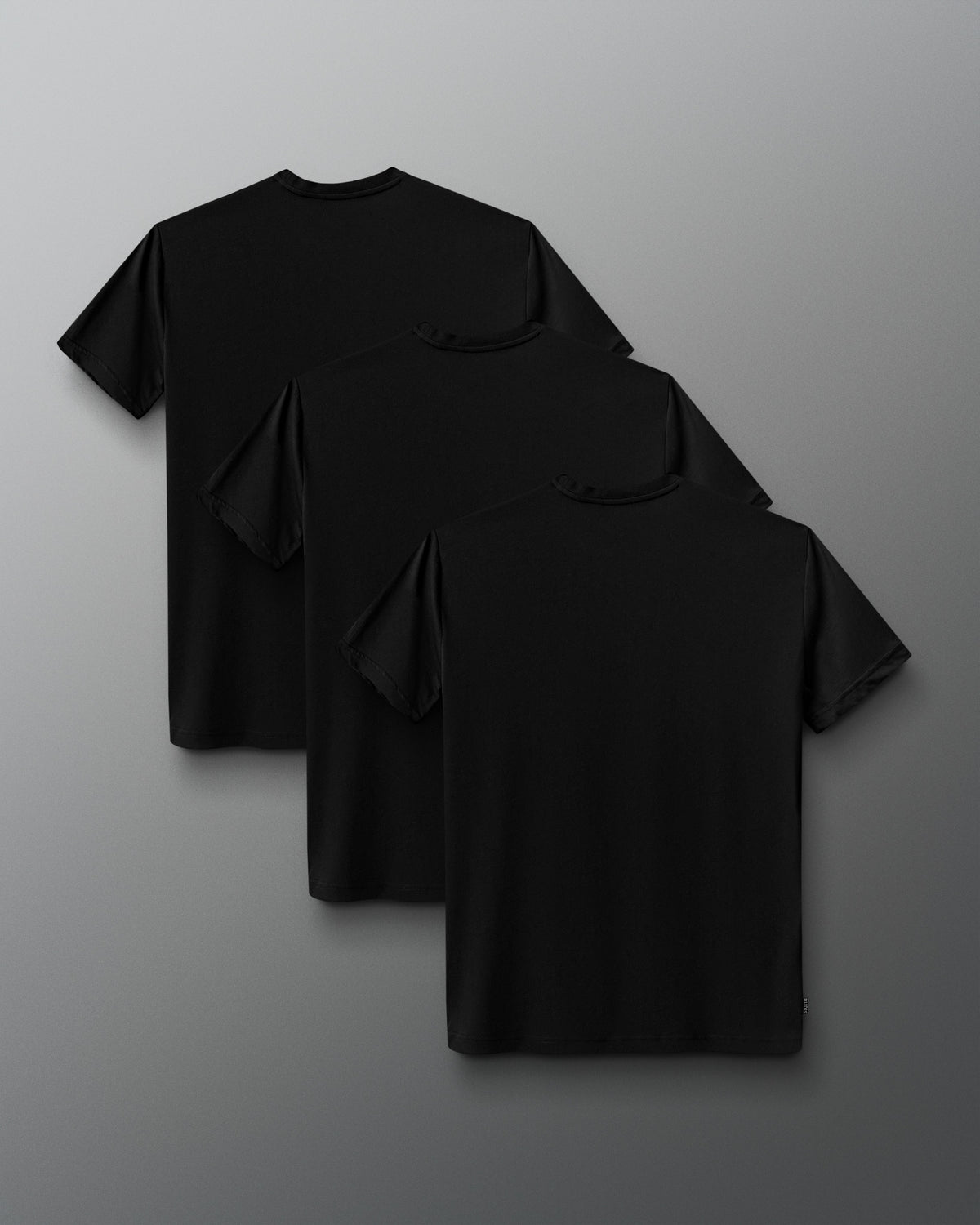 Three black short-sleeve crewneck t-shirts arranged in a cascading stack on a dark gray gradient background.