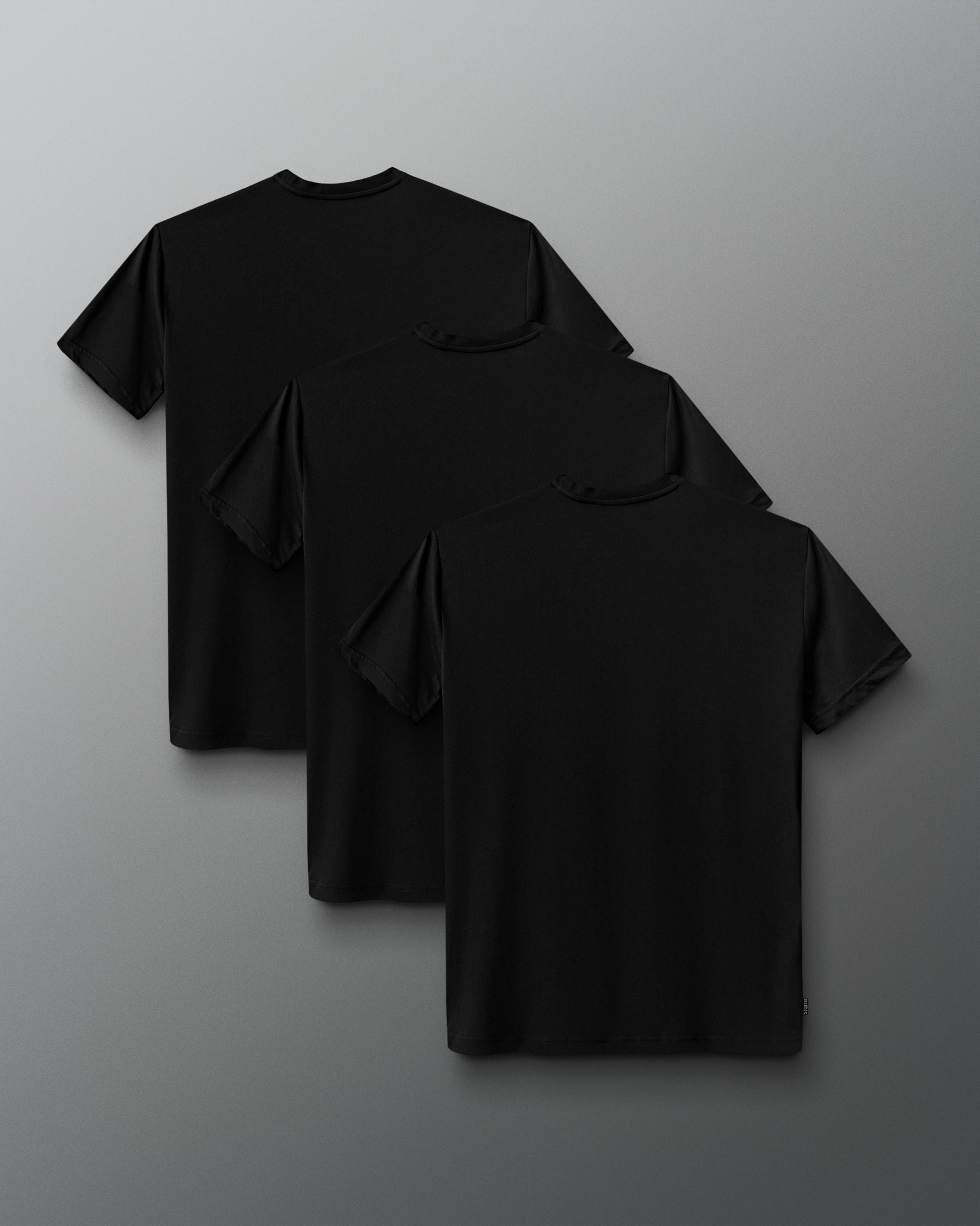Three black short-sleeve crewneck t-shirts arranged in a cascading stack on a dark gray gradient background.