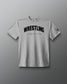 A light gray heather crewneck t-shirt featuring the word 'WRESTLING' in bold black arched letters across the chest, with 'A WAY OF LIFE' printed underneath in smaller text. A small black logo is visible on the left sleeve.
