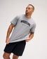 A man wearing a heather gray short-sleeve t-shirt with 'WRESTLING' printed in black across the chest, paired with black athletic shorts, against a light gray studio background.