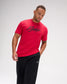 A man wearing a bright red short-sleeve t-shirt with a black 'RUDIS' logo across the chest, paired with black sweatpants, photographed against a light gray studio background.