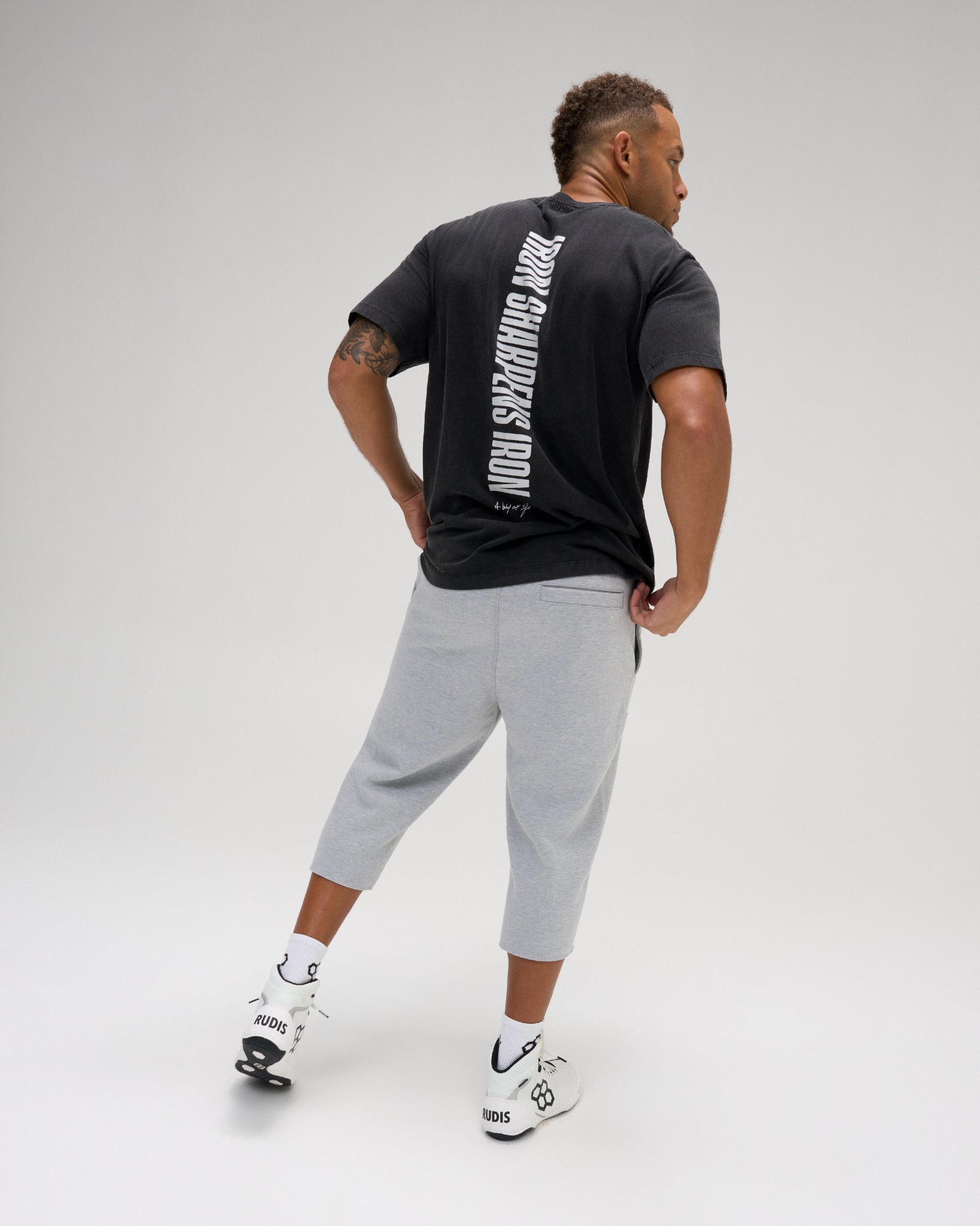 Back view of a model wearing the RUDIS Iron Sharpens Iron Classic Cotton T-Shirt in Washed Black, featuring a bold vertical white Iron Sharpens Iron graphic and classic short sleeves.